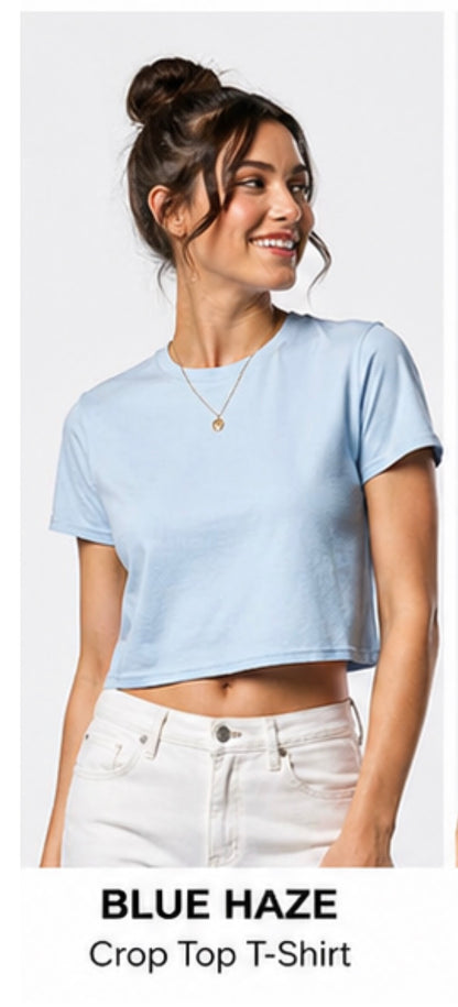 Woman wearing a light blue crop top t-shirt with text 'Blue Haze Crop Top T-Shirt' below.